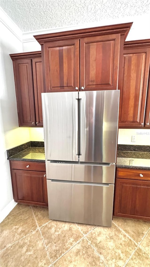 kitchen with dark stone countertops, stainless steel fridge, crown molding, and a textured ceiling