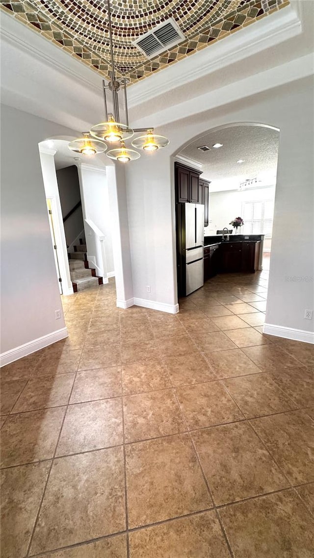 unfurnished dining area featuring tile patterned flooring, a textured ceiling, a raised ceiling, and ornamental molding