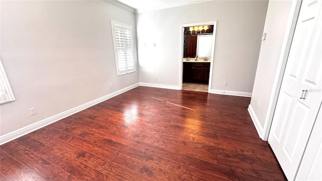 unfurnished bedroom featuring a closet, dark hardwood / wood-style flooring, ensuite bathroom, and crown molding