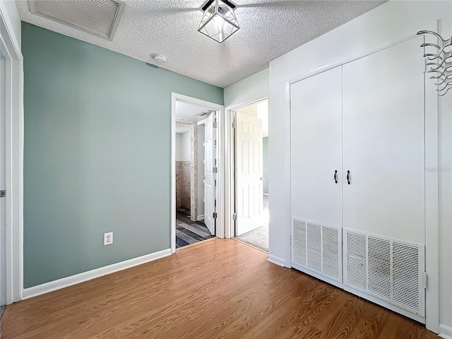 unfurnished bedroom featuring hardwood / wood-style flooring, ensuite bath, a textured ceiling, and a closet