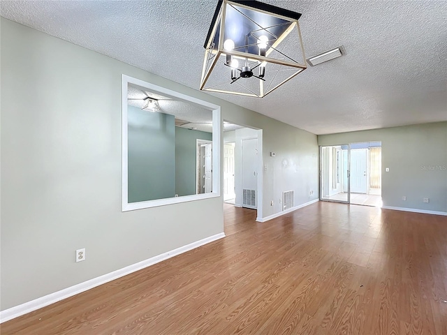 empty room with hardwood / wood-style floors, a chandelier, and a textured ceiling