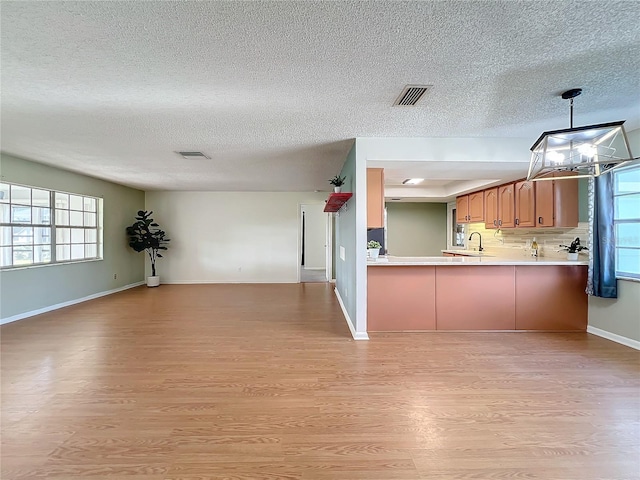 kitchen with tasteful backsplash, kitchen peninsula, light hardwood / wood-style floors, a textured ceiling, and decorative light fixtures