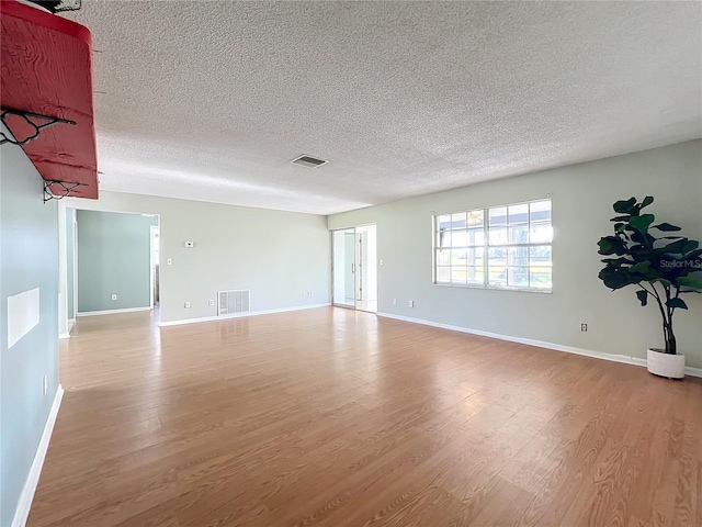 empty room with a textured ceiling and light hardwood / wood-style flooring