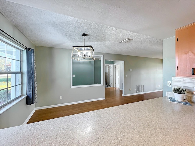 unfurnished dining area featuring a textured ceiling, hardwood / wood-style flooring, and an inviting chandelier