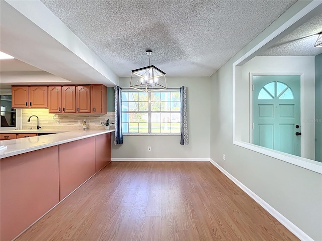 kitchen with backsplash, sink, light wood-type flooring, decorative light fixtures, and a chandelier