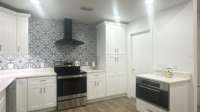 kitchen featuring wall chimney exhaust hood, white cabinetry, stainless steel appliances, and tasteful backsplash