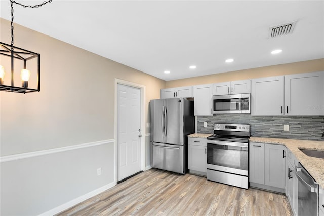 kitchen featuring hanging light fixtures, light stone counters, light hardwood / wood-style flooring, backsplash, and appliances with stainless steel finishes