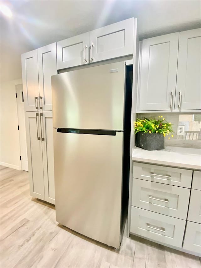 kitchen with white cabinets, stainless steel fridge, light hardwood / wood-style floors, and tasteful backsplash