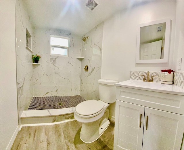 bathroom with a tile shower, vanity, toilet, and hardwood / wood-style floors