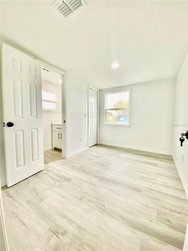 unfurnished bedroom featuring ensuite bath, light hardwood / wood-style flooring, and a textured ceiling