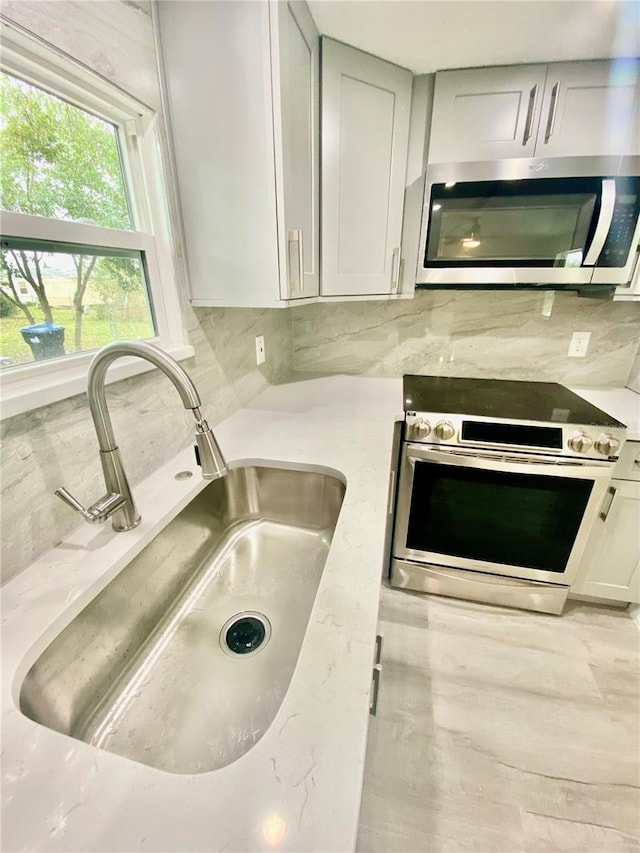 kitchen with decorative backsplash, appliances with stainless steel finishes, light stone counters, and sink