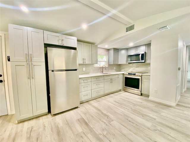 kitchen with backsplash, lofted ceiling with beams, sink, light wood-type flooring, and stainless steel appliances