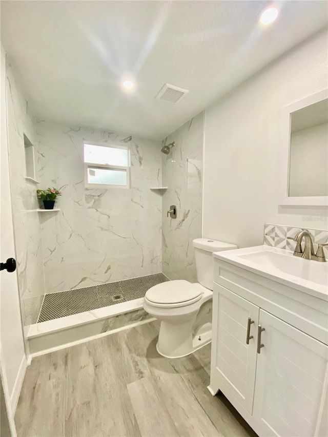 bathroom featuring wood-type flooring, vanity, a tile shower, and toilet