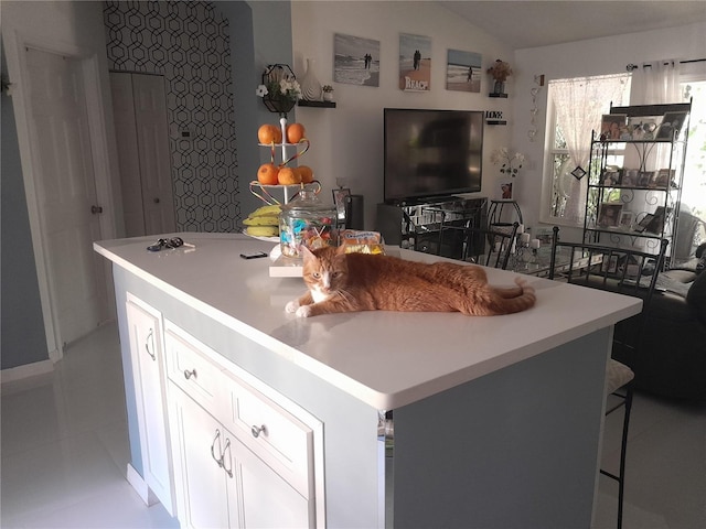 kitchen with lofted ceiling, light tile patterned floors, a center island, white cabinets, and a kitchen bar