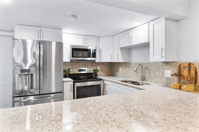 kitchen featuring light stone countertops, white cabinetry, stainless steel appliances, sink, and backsplash