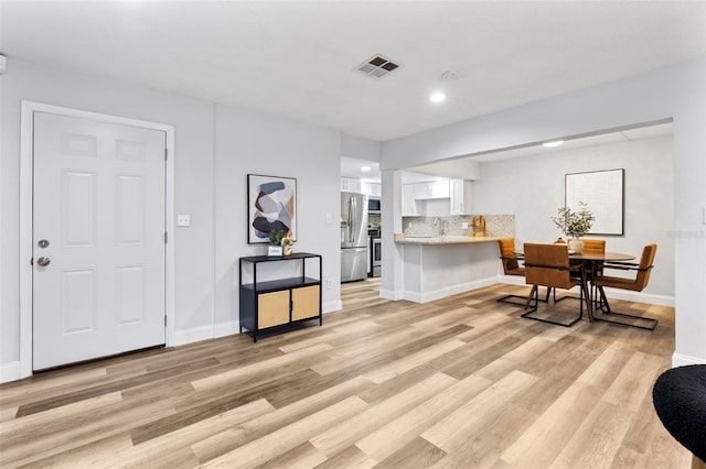 kitchen featuring backsplash, light hardwood / wood-style floors, kitchen peninsula, appliances with stainless steel finishes, and white cabinets