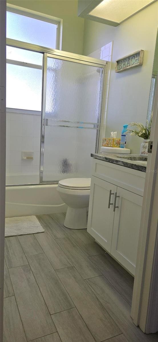 full bathroom with enclosed tub / shower combo, vanity, and toilet