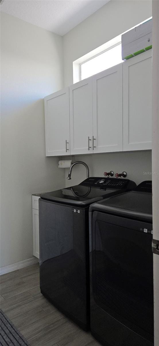 laundry area featuring cabinets, hardwood / wood-style flooring, and washing machine and clothes dryer