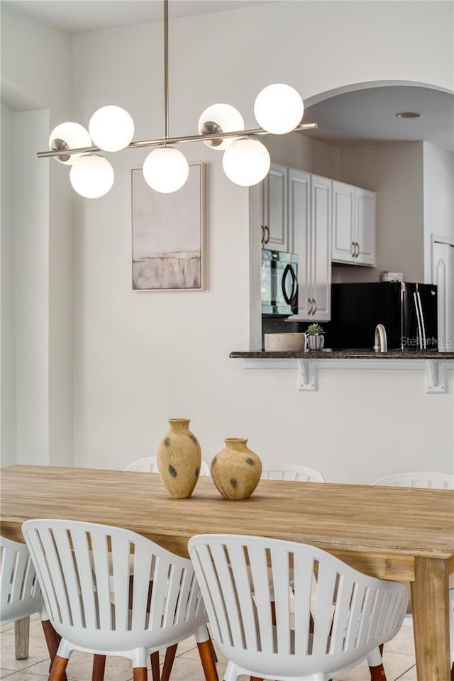 kitchen featuring hanging light fixtures, light tile patterned floors, kitchen peninsula, black refrigerator, and white cabinets