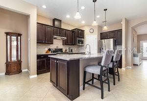 kitchen featuring pendant lighting, decorative backsplash, a center island with sink, and sink