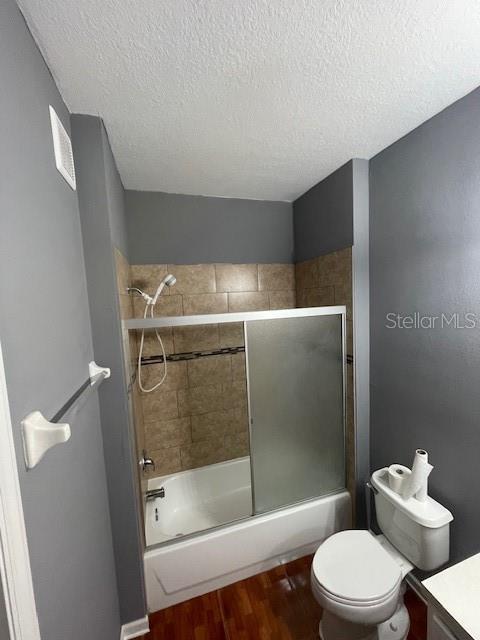 full bathroom featuring toilet, wood-type flooring, bath / shower combo with glass door, a textured ceiling, and vanity