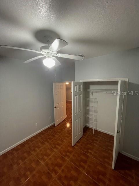 unfurnished bedroom with ceiling fan, a textured ceiling, and a closet