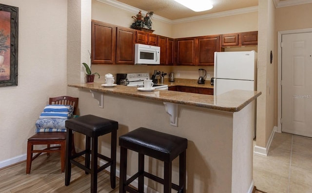 kitchen featuring a breakfast bar area, kitchen peninsula, crown molding, and white appliances