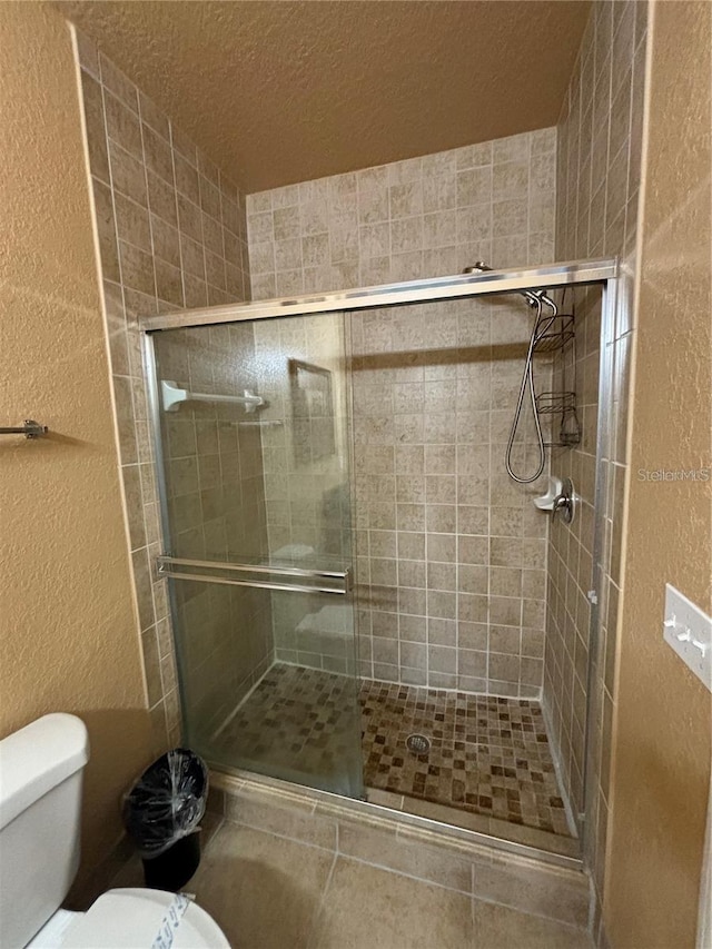 bathroom with toilet, a shower with shower door, and a textured ceiling