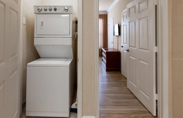 clothes washing area featuring stacked washer and dryer, crown molding, and light hardwood / wood-style floors