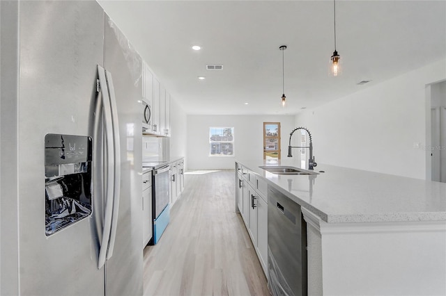 kitchen featuring stainless steel appliances, sink, white cabinets, hanging light fixtures, and an island with sink