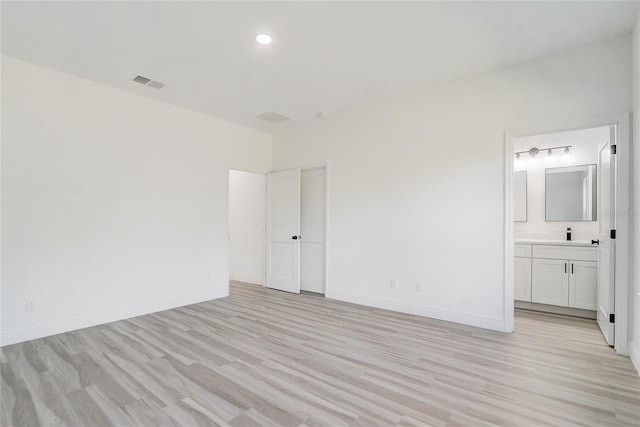 unfurnished bedroom with ensuite bathroom and light wood-type flooring