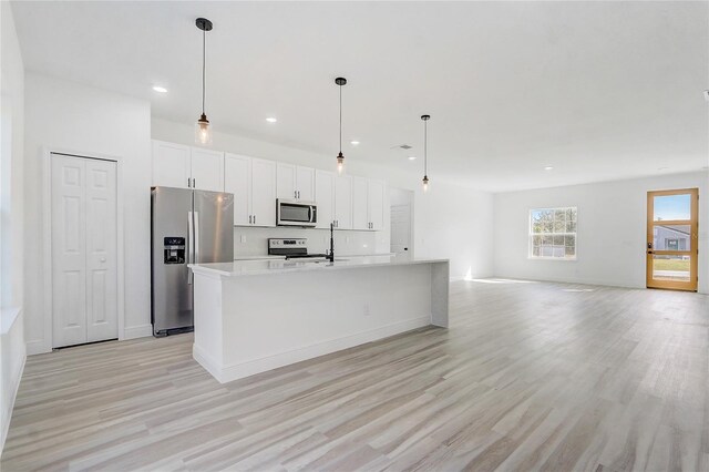 kitchen featuring decorative light fixtures, white cabinetry, an island with sink, and appliances with stainless steel finishes