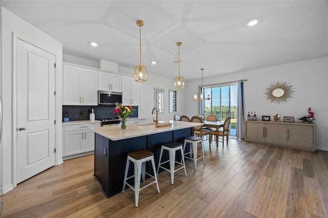 kitchen with an island with sink, pendant lighting, a breakfast bar, white cabinets, and appliances with stainless steel finishes