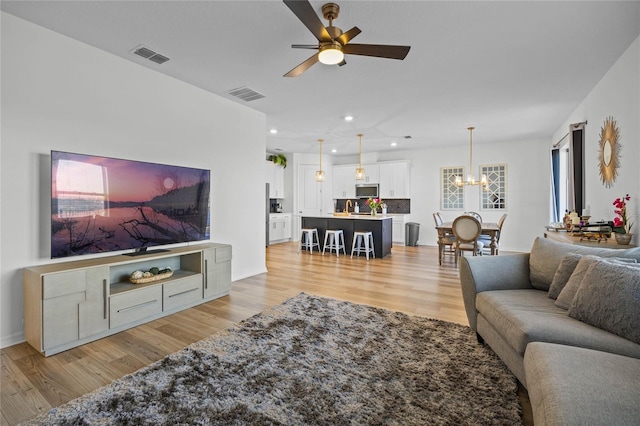 living room with ceiling fan with notable chandelier and light hardwood / wood-style flooring