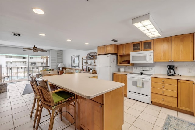 kitchen featuring ceiling fan, a center island, white appliances, a breakfast bar area, and light tile patterned floors