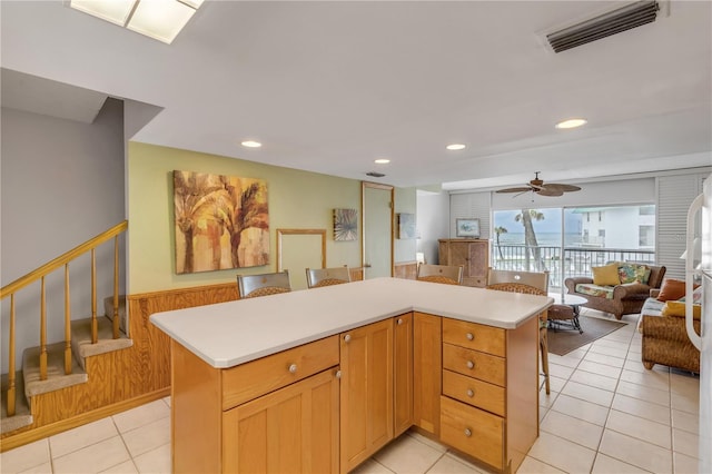 kitchen with a center island, a kitchen breakfast bar, wooden walls, ceiling fan, and light tile patterned floors