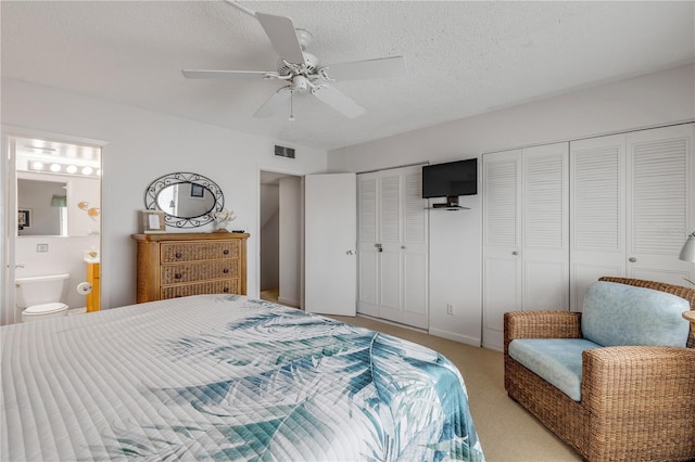 carpeted bedroom featuring a textured ceiling, ensuite bath, ceiling fan, and multiple closets