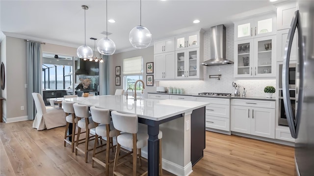 kitchen featuring white cabinetry, a kitchen island with sink, pendant lighting, and wall chimney exhaust hood