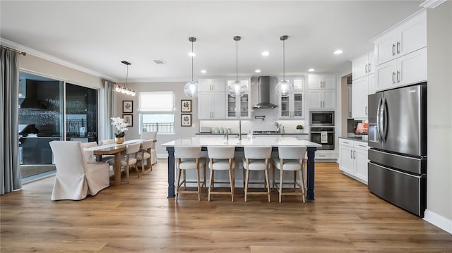 kitchen with stainless steel appliances, wall chimney range hood, pendant lighting, and white cabinetry