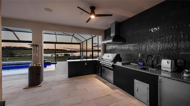 patio terrace at dusk with an outdoor kitchen, grilling area, glass enclosure, ceiling fan, and sink