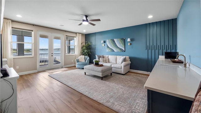 living room with light hardwood / wood-style floors, a water view, ceiling fan, french doors, and sink