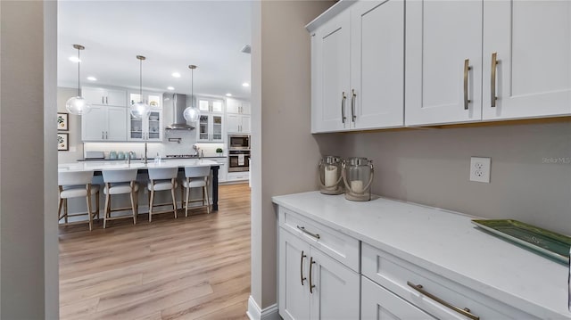 kitchen featuring white cabinetry, stainless steel microwave, pendant lighting, and wall chimney range hood