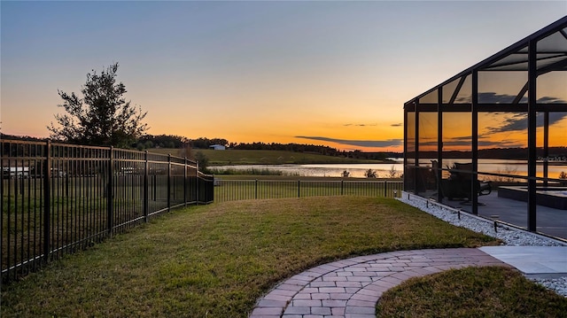 yard at dusk featuring a water view, glass enclosure, and a patio area