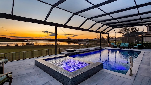 pool at dusk with a lanai, a patio area, pool water feature, an in ground hot tub, and a water view