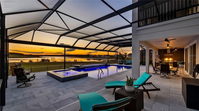 patio terrace at dusk featuring a pool with hot tub, ceiling fan, glass enclosure, and a water view