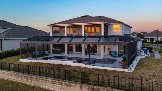 back house at dusk with a balcony, a lawn, a pool with hot tub, and a patio area