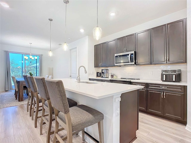 kitchen with sink, a center island with sink, a kitchen breakfast bar, pendant lighting, and stainless steel appliances