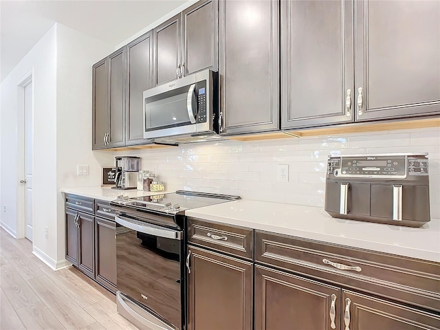 kitchen with light stone counters, backsplash, light hardwood / wood-style flooring, and appliances with stainless steel finishes