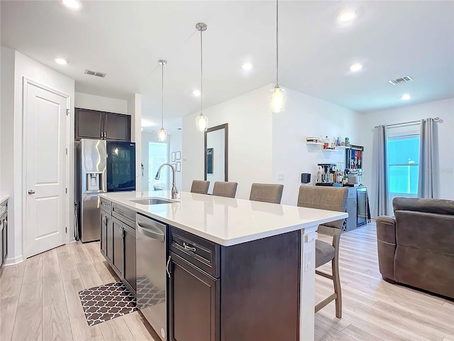 kitchen with sink, appliances with stainless steel finishes, a kitchen island with sink, a kitchen bar, and decorative light fixtures