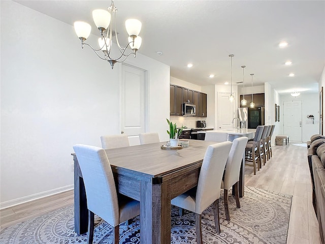 dining space with sink, a chandelier, and light wood-type flooring